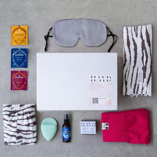 Restore and Go Box with loungewear, gym shorts, sleep mask, magnesium spray, bamboo charcoal soap, exfoliating mitt, calming tea, and handwritten message.